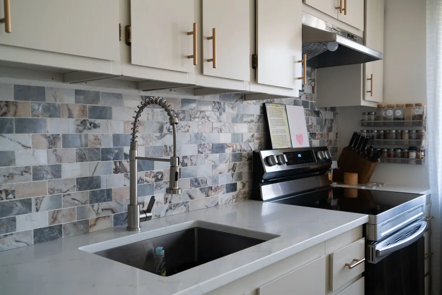 Compact ADU kitchen with cream cabinetry and a mosaic tile backsplash
