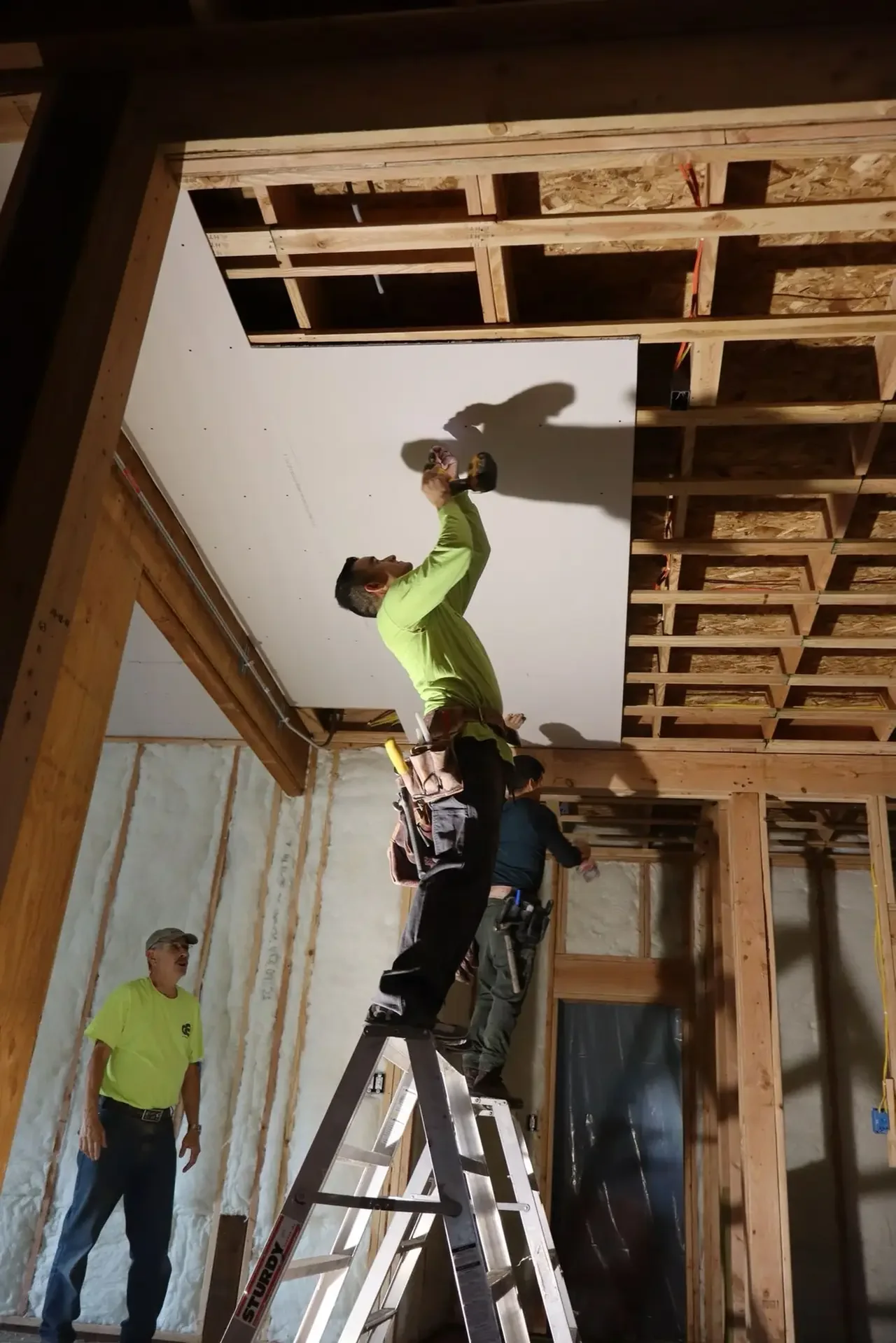 JR Drywall crew member hanging board on a ceiling with the joists still exposed