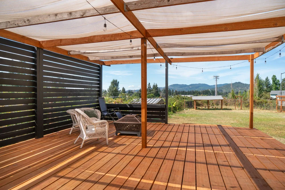 Deck seating area beneath a pergola with a horizontal slat privacy screen