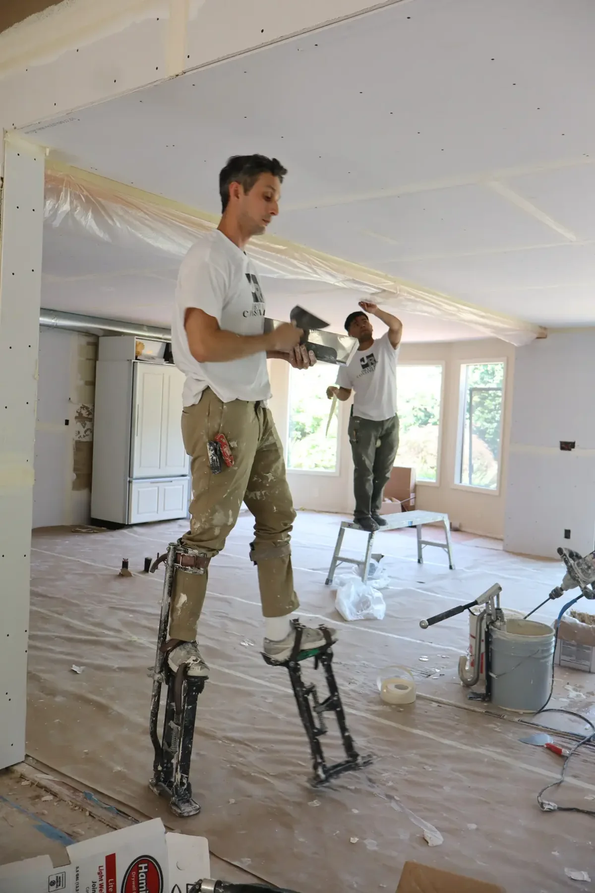 Two JR Drywall crew members on stilts finishing a ceiling